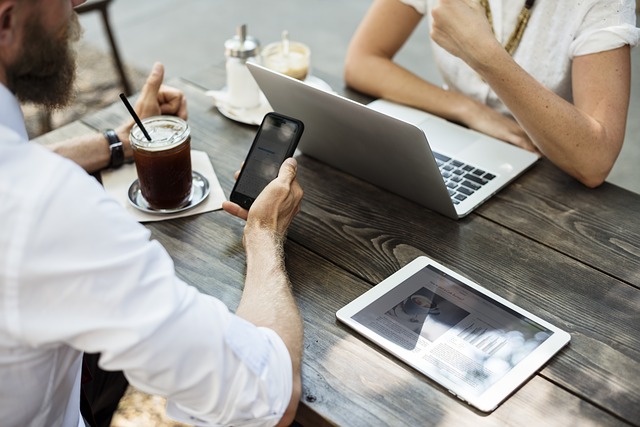 posezení venku u kávy, muž drží telefon v ruce, žena má před sebou notebook, na stole leží tablet.jpg